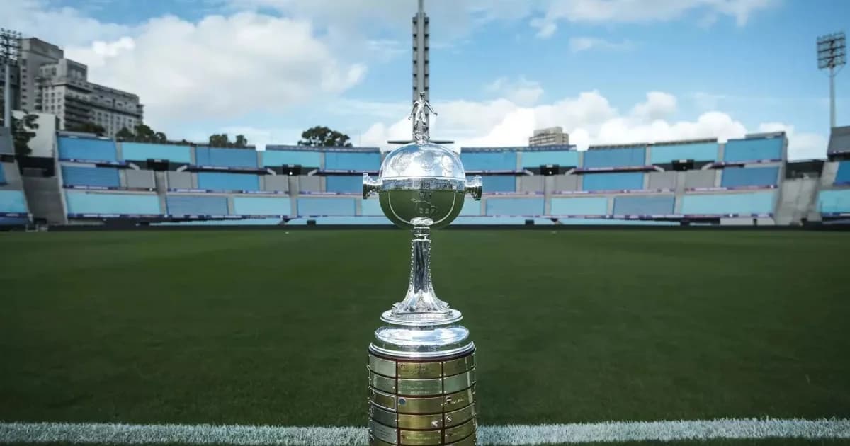 Estádio ao entardecer com placar em contagem regressiva, técnico e jogadores de costas, tensão pelo prazo da Libertadores