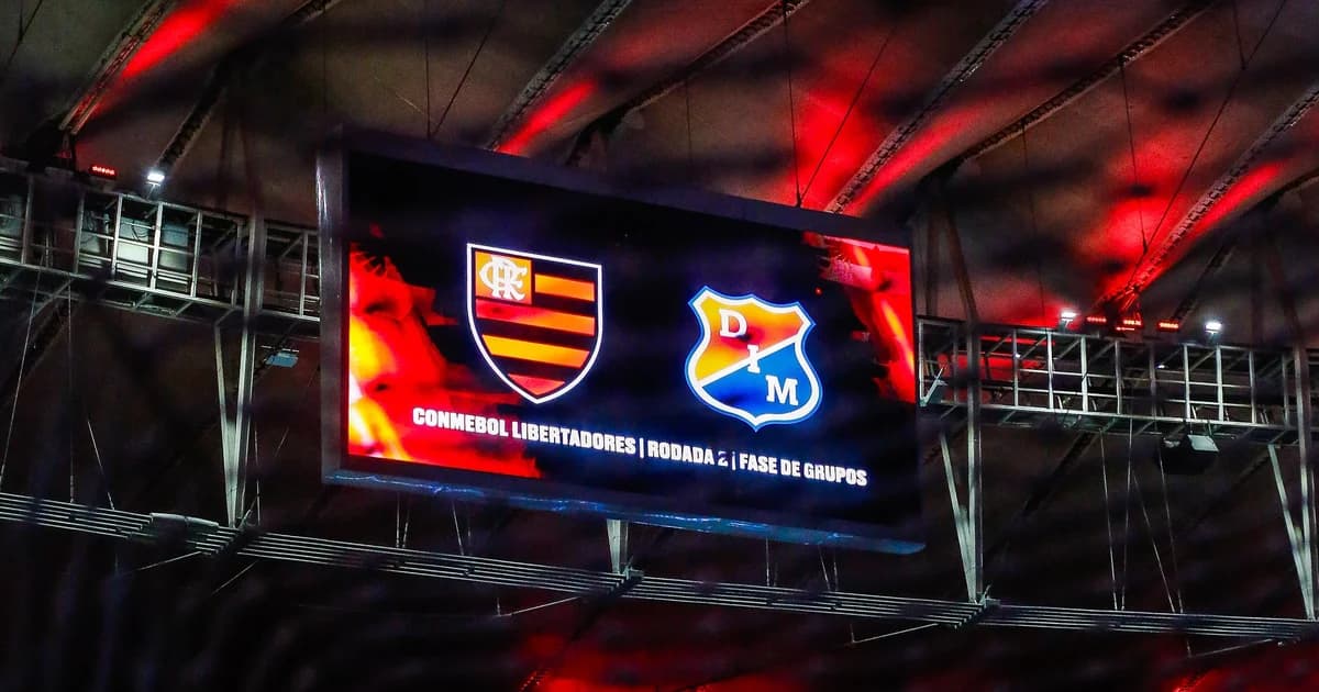 Estádio noturno: treinador anuncia 21 convocados, torcida vibrante e três figuras com faixa representando desfalques na Libertadores.