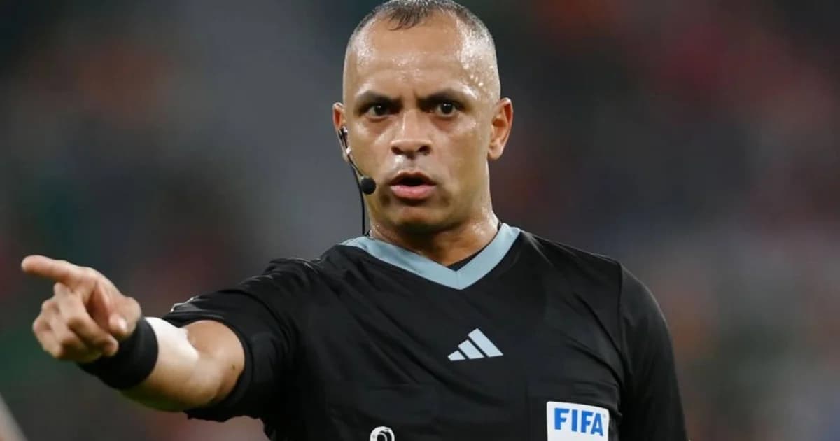 Árbitro de costas no Maracanã, apito erguido, bola em jogo e torcida dividida em cores do clássico