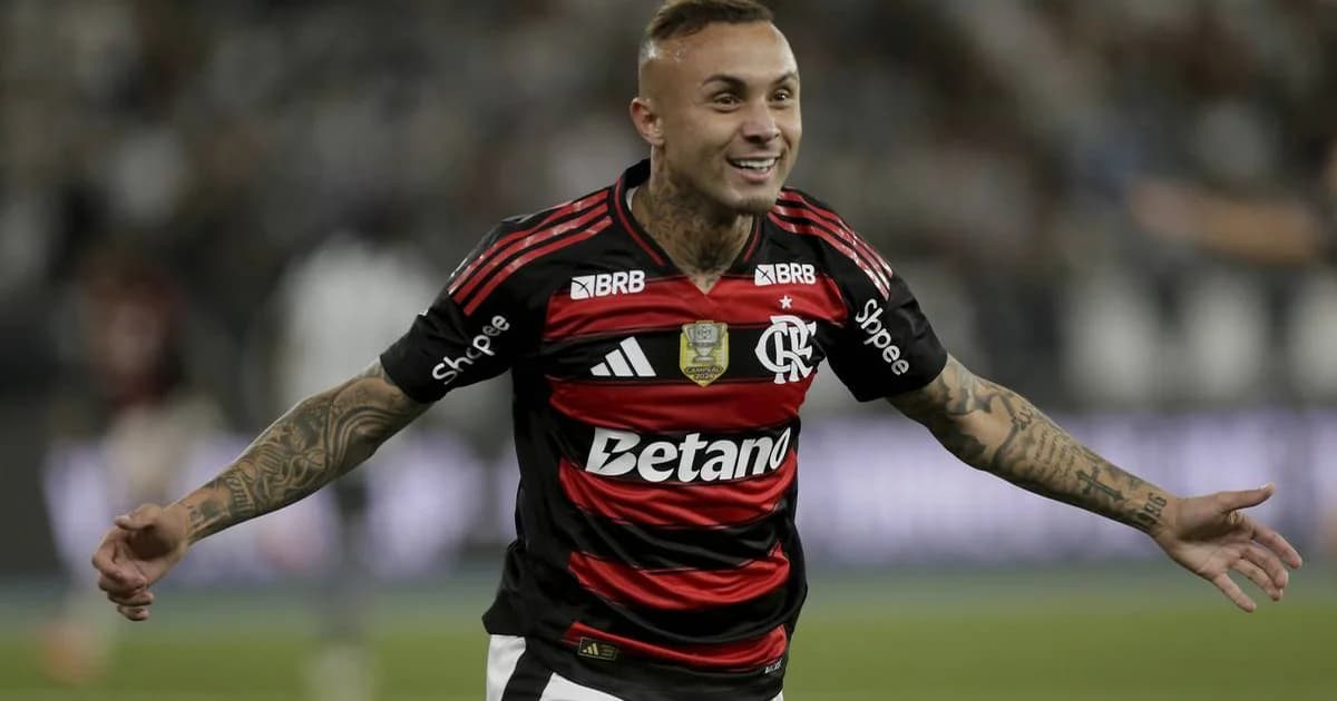 Everton Cebolinha de costas no gramado segurando contrato, luzes do estádio e atmosfera de negociação com clube carioca.