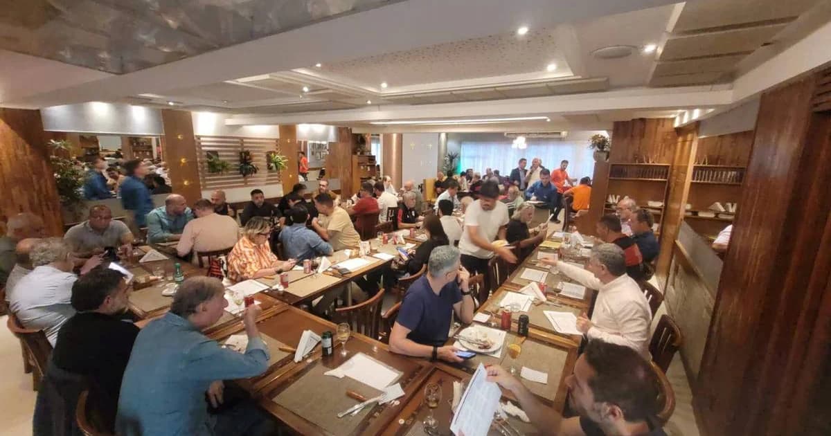 Conselheiros do Flamengo reunidos à noite em restaurante, mesa com laptops e projeção sobre gestão e modernização, estádio ao fundo