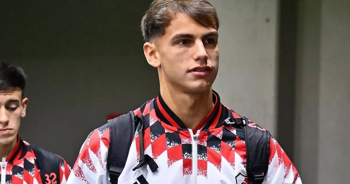 Atacante argentino desembarca no Galeão com cachecol vermelho e preto, cercado por imprensa e torcedores; chegada ao Flamengo.