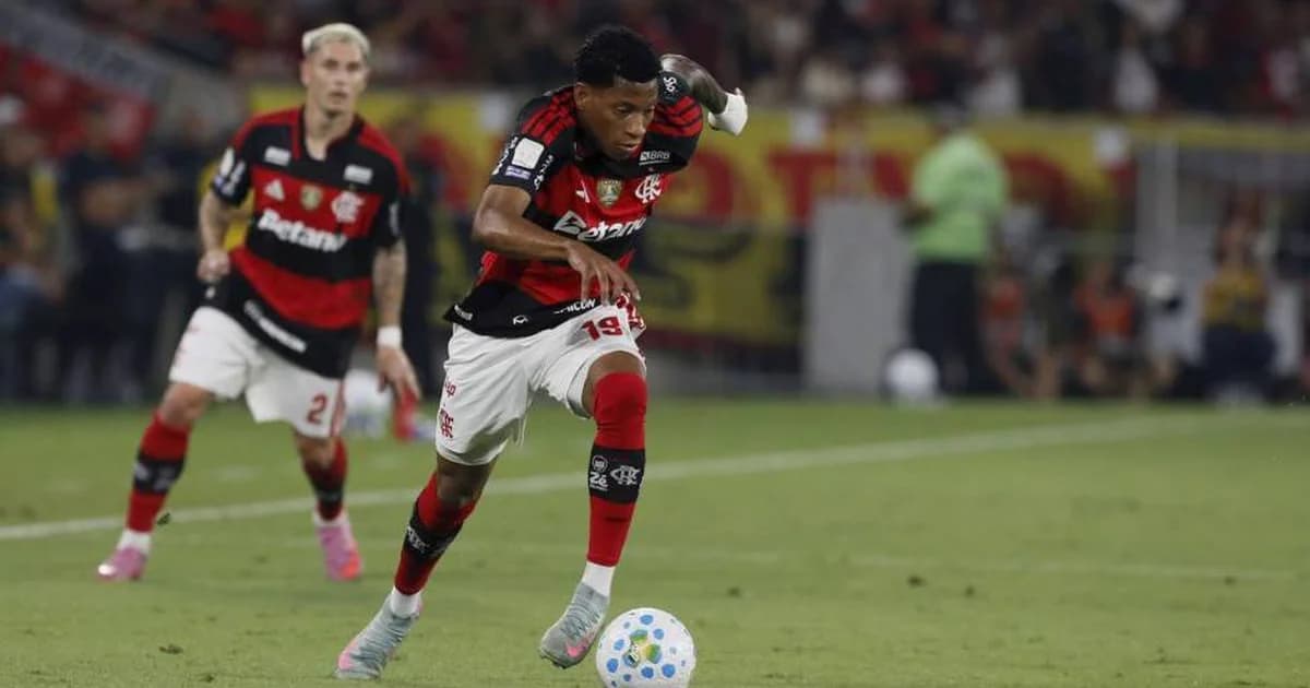 Atacante do Flamengo desembarca no Brasil no aeroporto, vestido de vermelho e preto, torcida ao fundo, clima de foco e determinação