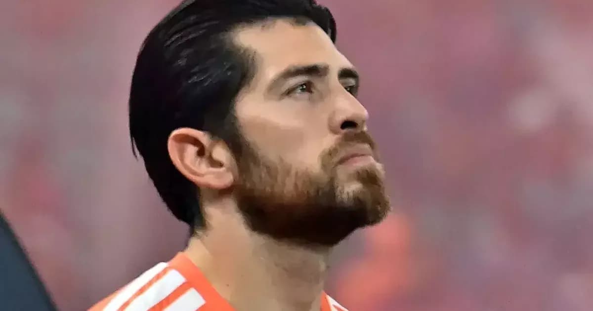 Goleiro visto por trás em estádio ao entardecer, torcida em vermelho e preto desfocada, simbolizando pressão e busca por estabilidade.