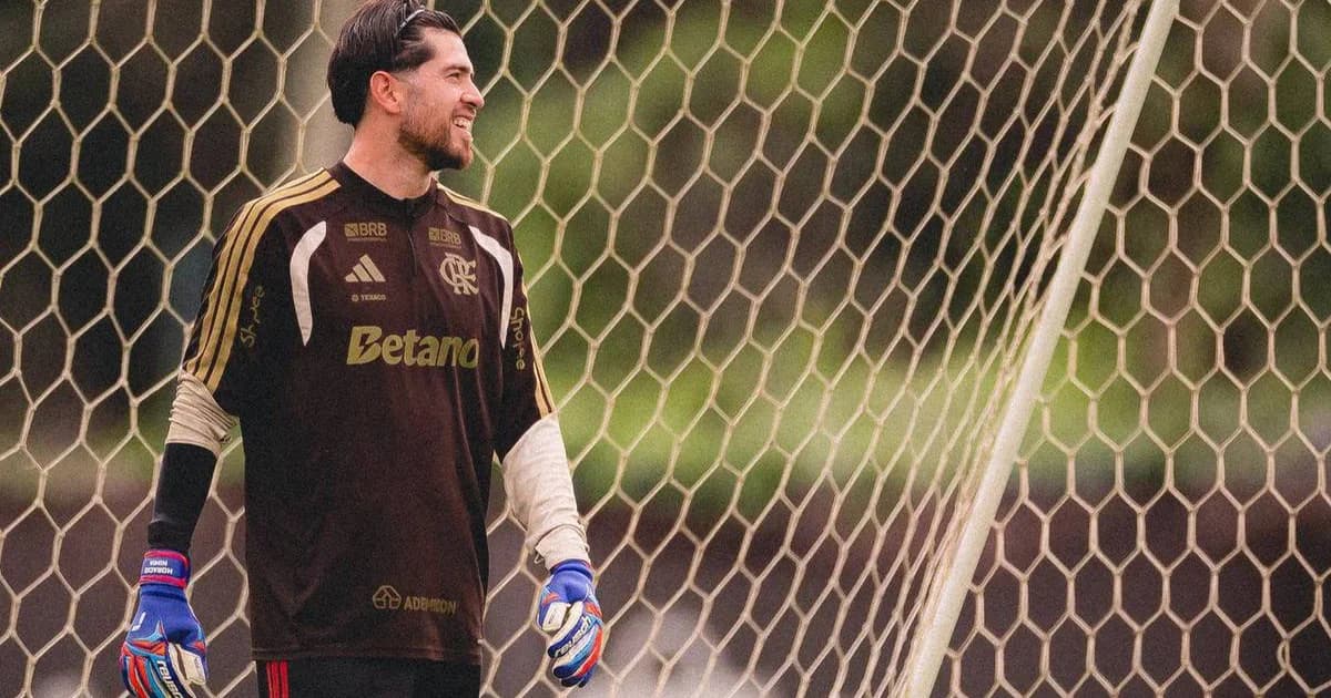 Goleiro do Flamengo em frente ao gol, sereno diante da pressão e críticas da torcida em estádio lotado ao entardecer.