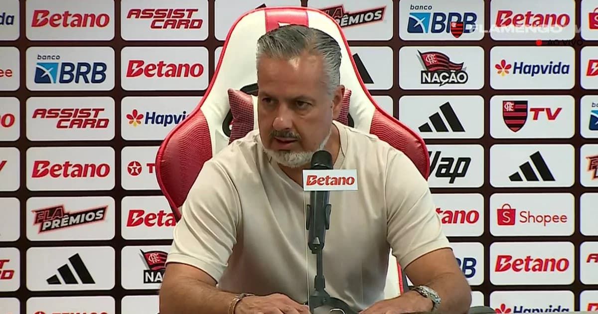 Dirigente do Flamengo gesticula criticando arbitragem ao lado de gramado irregular após empate, torcida e estádio ao fundo.