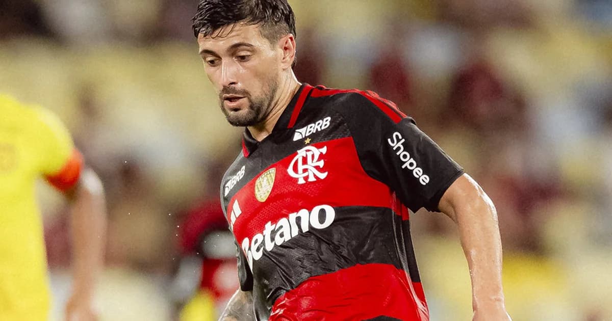 Atacante do Flamengo comemora 100 gols em estádio lotado com torcida em vermelho e preto, confetes e placar mostrando '100'.