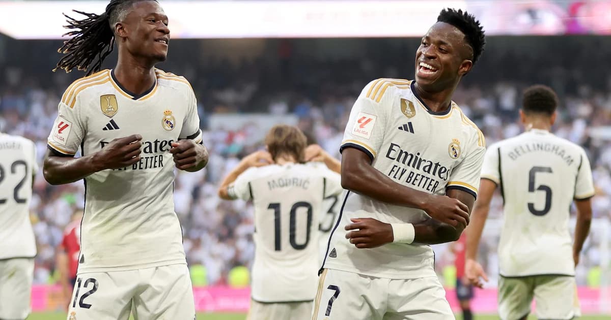 Dois jogadores anônimos se abraçam no túnel do estádio; silhuetas de astros brasileiros ao fundo — amizade entre Camavinga e Vini Jr.