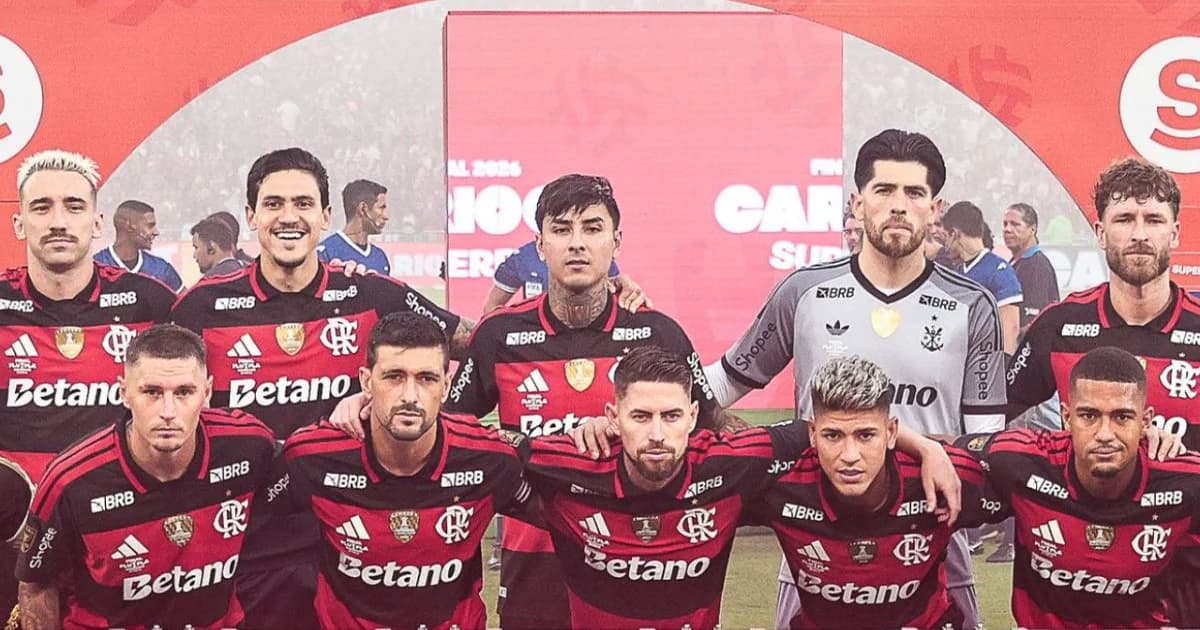 Estádio com jogadores anônimos sob sombra simbólica de acusação; torcida em vermelho e preto, imprensa, microfones e tensão midiática.
