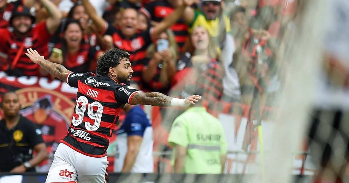 Atacante de costas no gramado, torcida em vermelho e preto ao fundo e contrato rasgado, clima de saudade e desejo de retorno.