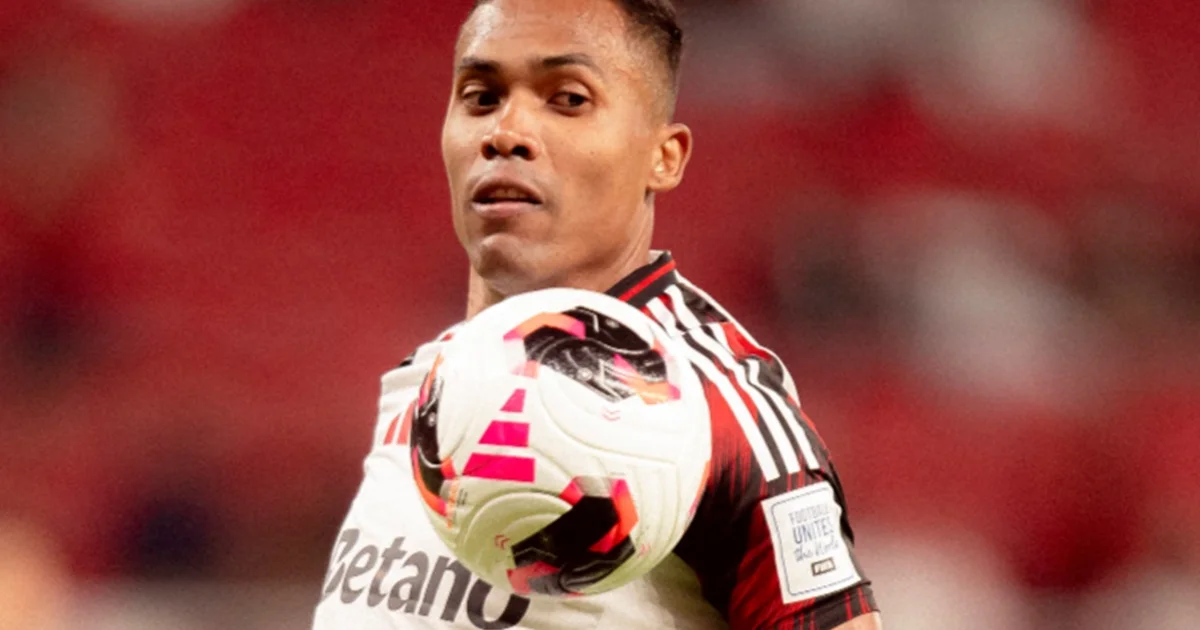 Lateral-esquerdo veterano à beira do campo, calendário e avião sobrepostos, estádio iluminado; transmite exaustão, viagem e dúvida sobre permanência.