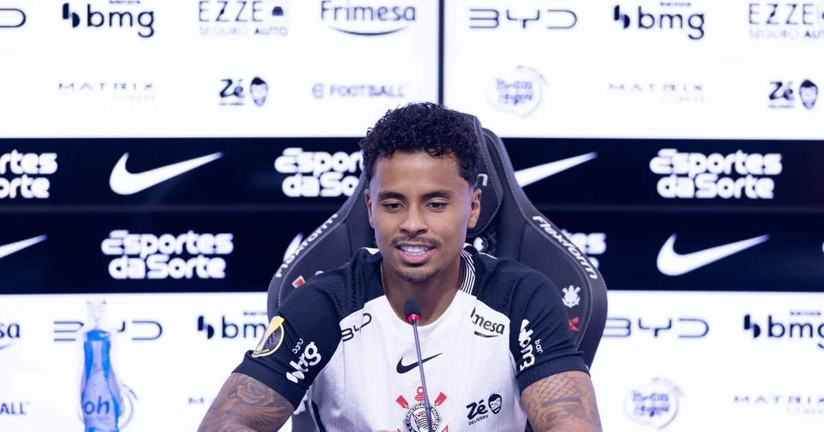 Allan apresentado pelo Corinthians após saída do Flamengo: meio-campista em coletiva, estádio e torcida ao fundo, clima de mudança.