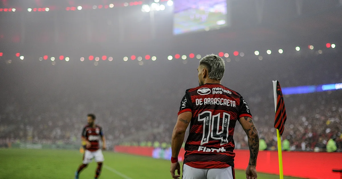 Arrascaeta capitão com a camisa 14 do Flamengo no estádio em homenagem a ídolo do basquete, torcida ao fundo.
