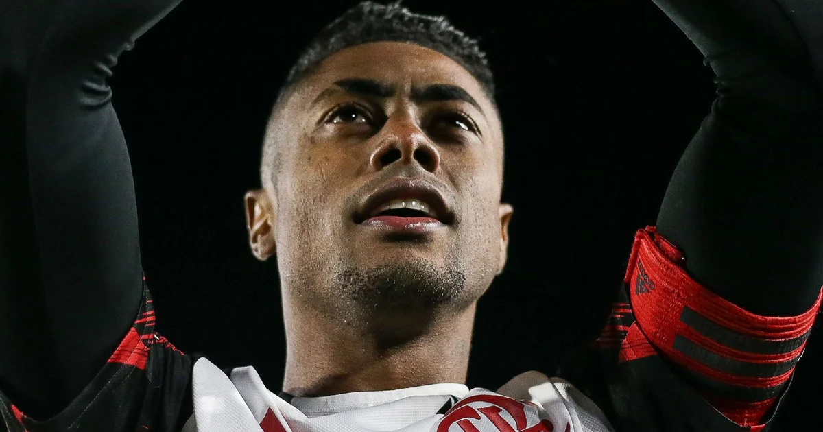 Atacante assinando renovação de contrato no estádio, torcida ao fundo com faixas e confetes — renovação do Flamengo até 2027