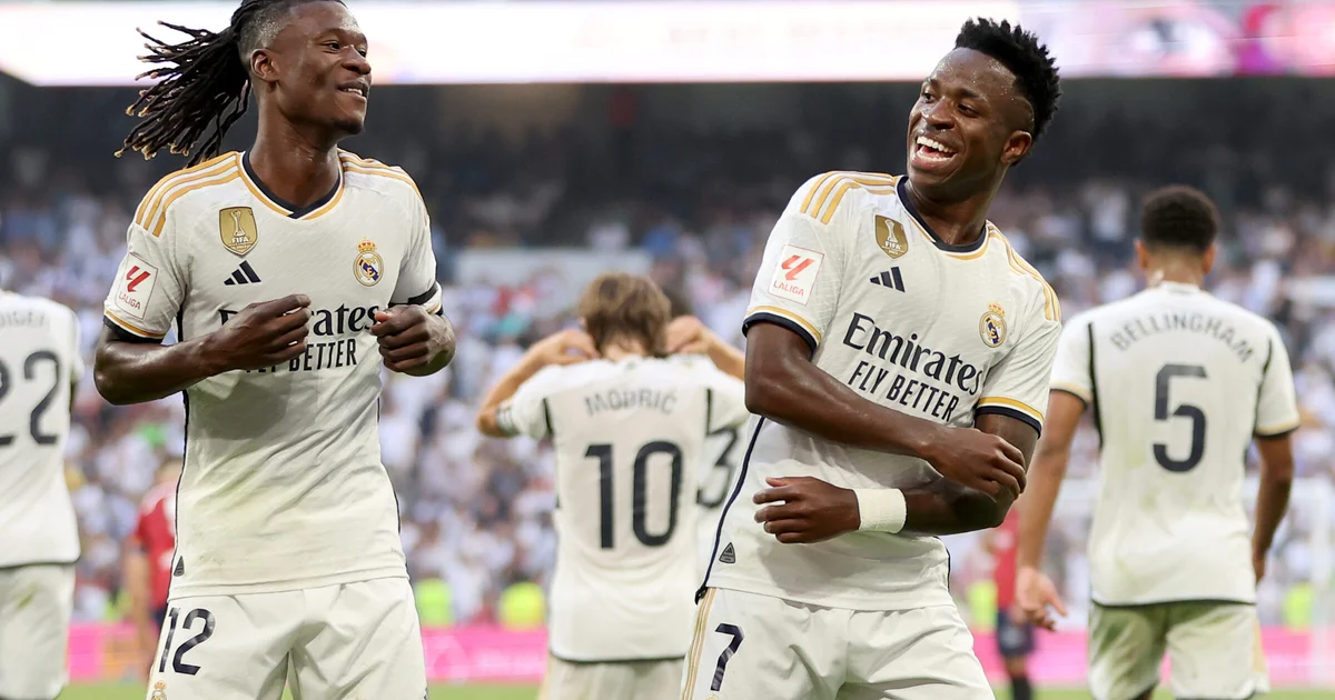 Dois jogadores anônimos se abraçam no túnel do estádio; silhuetas de astros brasileiros ao fundo — amizade entre Camavinga e Vini Jr.
