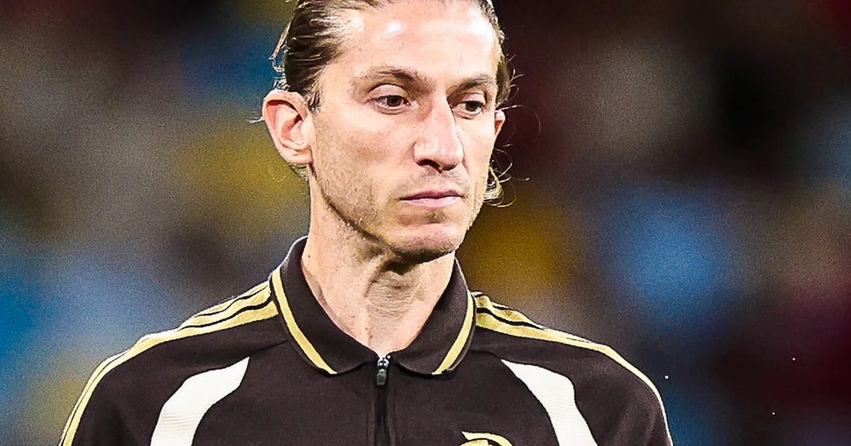 Treinador de costas em estádio vazio com prancheta tática, passaporte e livros, simbolizando plano e estudos rumo à Europa