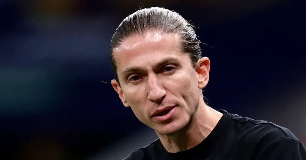 Treinador Filipe Luís saindo do estádio após vitória por 8 a 0, mala na mão e horizonte europeu ao fundo, torcida surpresa.