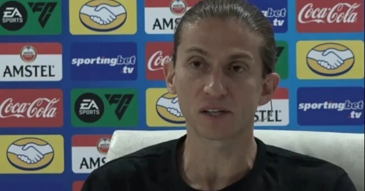 Técnico apoia atacante negro na lateral do estádio, torcida ao fundo com faixas contra o racismo, clima de solidariedade e denúncia