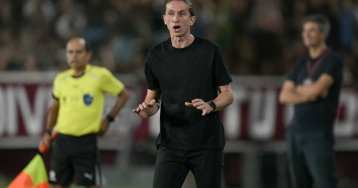 Treinador anônimo em coletiva pós-derrota no estádio, microfones à frente; ilustração sobre acusação de racismo e clima tenso.