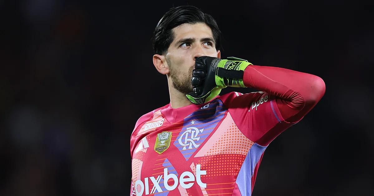 Jogador de costas com uniforme vermelho e preto em estádio de Buenos Aires, torcida ao fundo; clima tenso antes da Recopa.