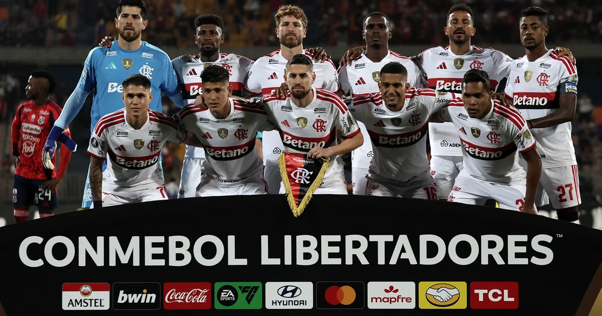Placar com 'W.O.' no estádio, silhuetas em vermelho e preto comemoram possível classificação do Flamengo na Libertadores.