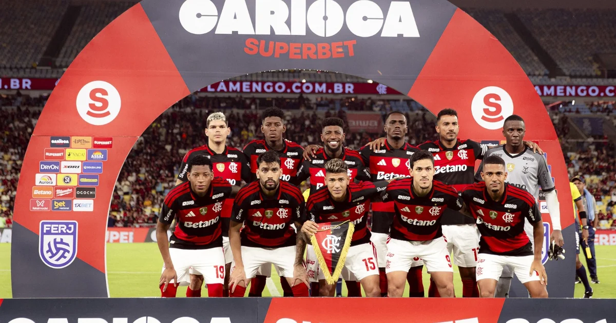 Jogador assinando contrato em estádio com cores do Flamengo (rubro-negro), escudo abstrato simboliza blindagem até 2030.