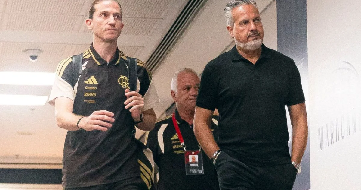 Diretor do Flamengo aponta prancheta tática no centro de treinamento, clima tenso, imprensa e estádio ao fundo