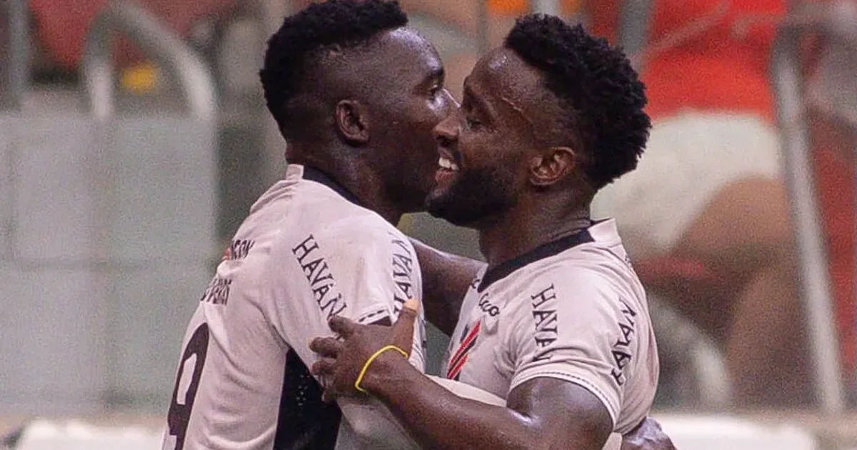 Estádio ao entardecer em tons vermelho e preto, silhueta de atacante camisa 9, contrato de transferência e torcida animada