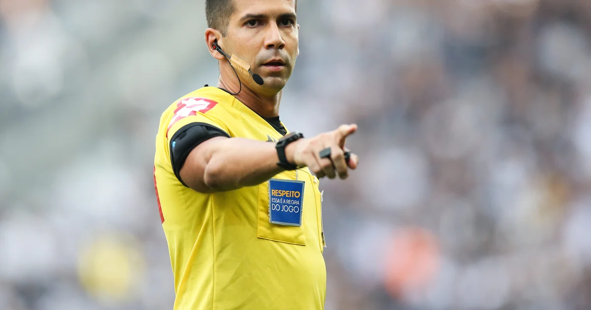 Árbitro não identificável no Maracanã, torcida do Flamengo em vermelho e preto e adversária em verde e grená, clima tenso e dramático.