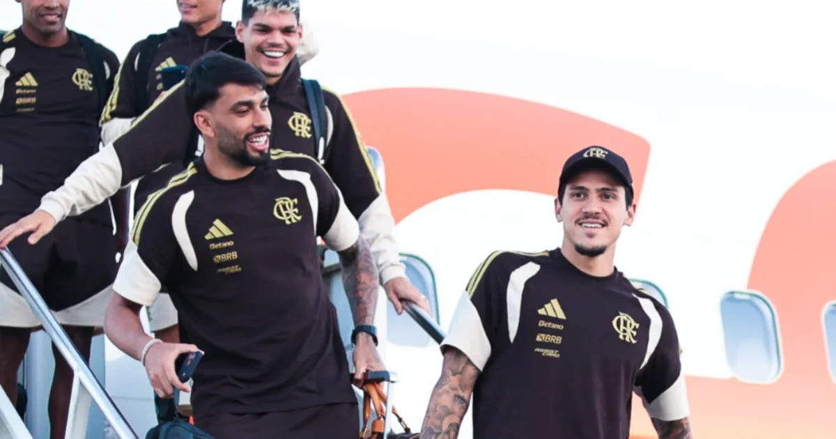 Delegação do Flamengo desembarca em Buenos Aires ao entardecer; torcida com bandeiras e estádio iluminado ao fundo para a Recopa.