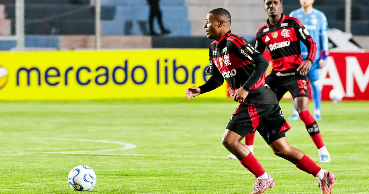 Maracanã ao entardecer: meio-campo vazio antes do clássico, roupas vermelhas e pretas sem logos, equipe médica e clima tenso