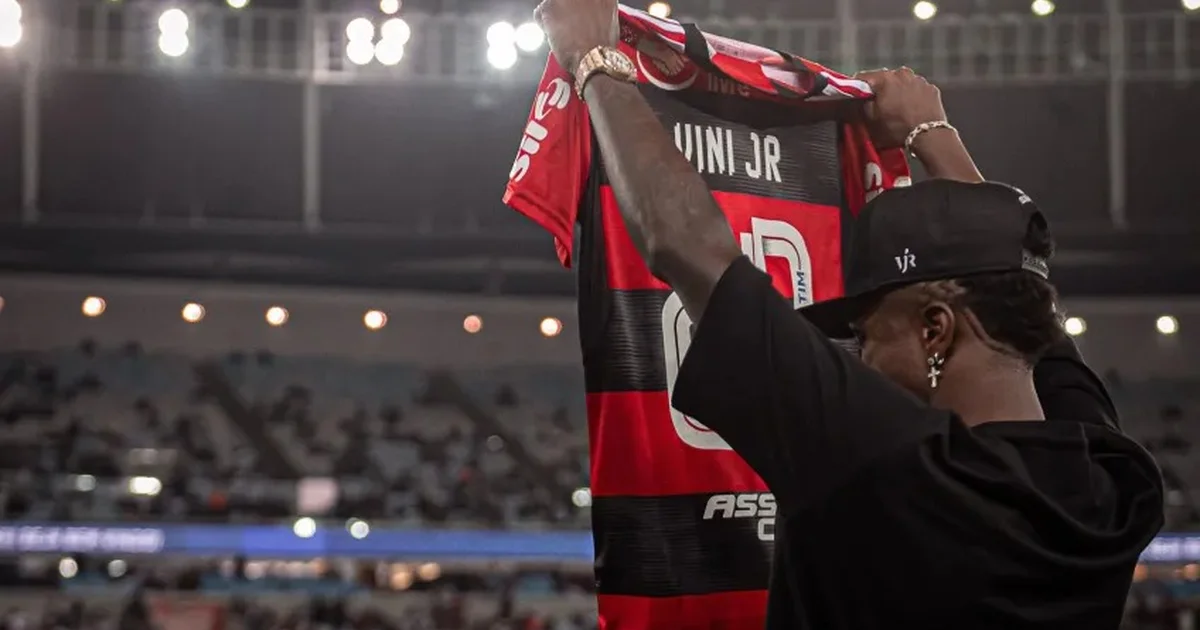 Ilustração: torcida com mosaico 'Não ao racismo' e jogador negro em silhueta erguendo o punho, homenagem a Vini Jr e denúncia ao racismo.