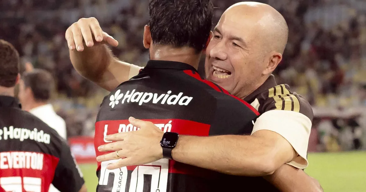 Novo treinador abraçado pelo elenco do Flamengo na comemoração do título, estádio iluminado com confetes vermelhos e pretos.