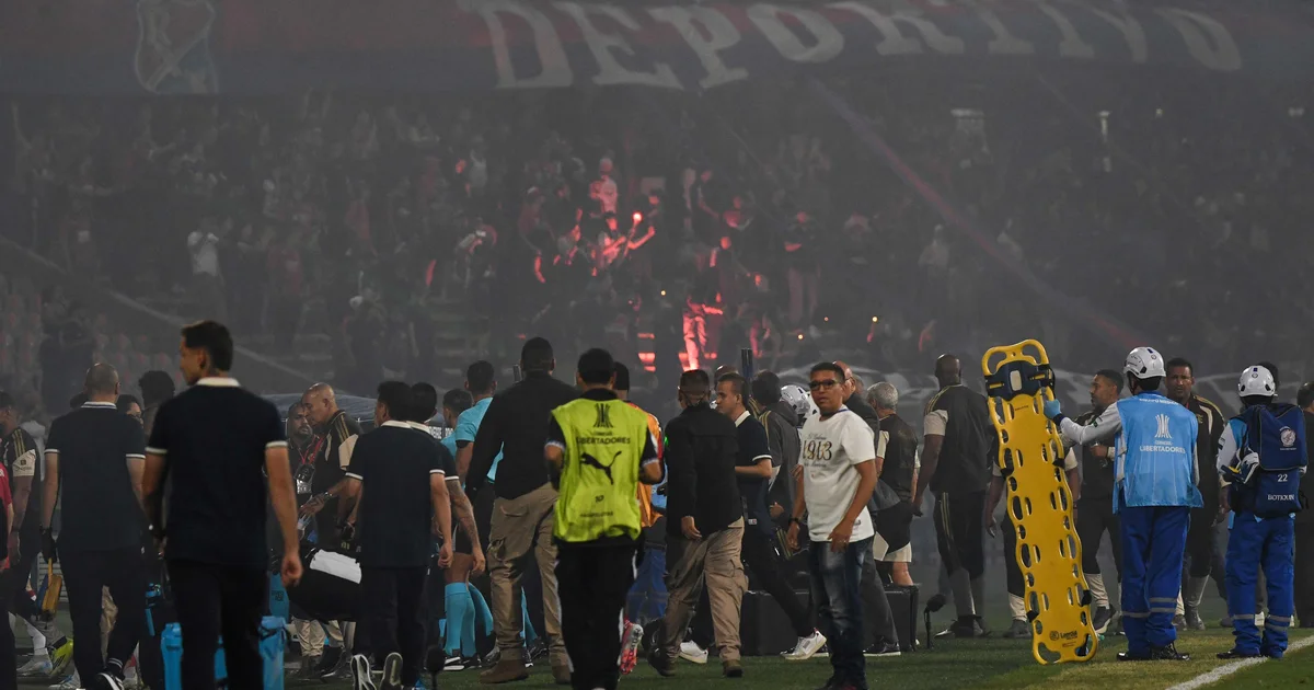 Estádio em tumulto com fumaça e torcedores anônimos; partida Independiente Medellín x Flamengo cancelada