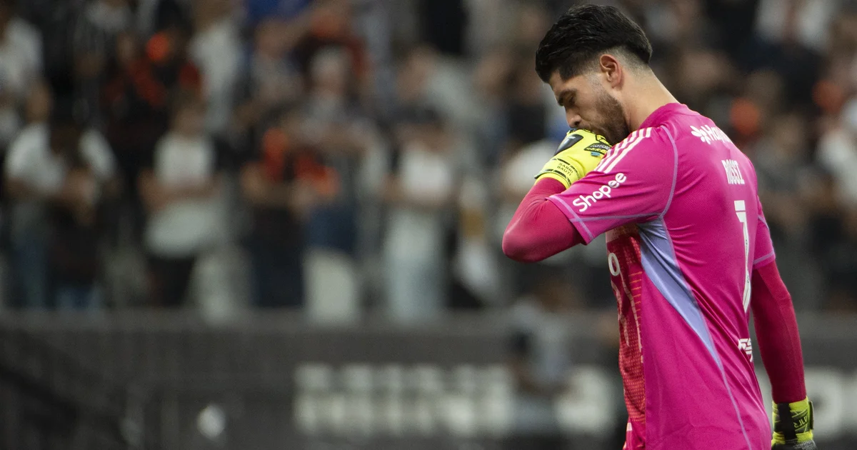 Goleiro de costas em estádio lotado, contrato transparente e técnico em silhueta, torcida e cores vermelho e preto.
