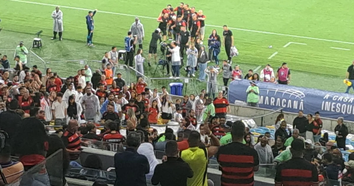 Homem negro no gramado do Maracanã diante de torcida hostil, simbolizando hostilização e racismo, multidão desfocada e atmosfera tensa.