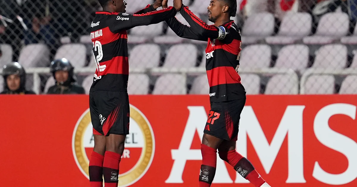 Estádio noturno da Libertadores: jogadores em silhueta celebram vitória do Flamengo por 2 a 0, torcida em vermelho e preto