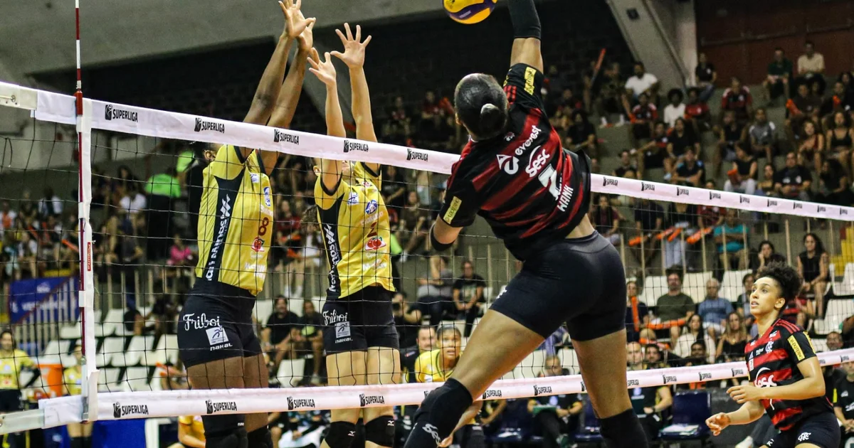Jogadora do Flamengo no ar atacando na Superliga de vôlei, torcida rubro-negra vibrando na arena em clima de playoff.