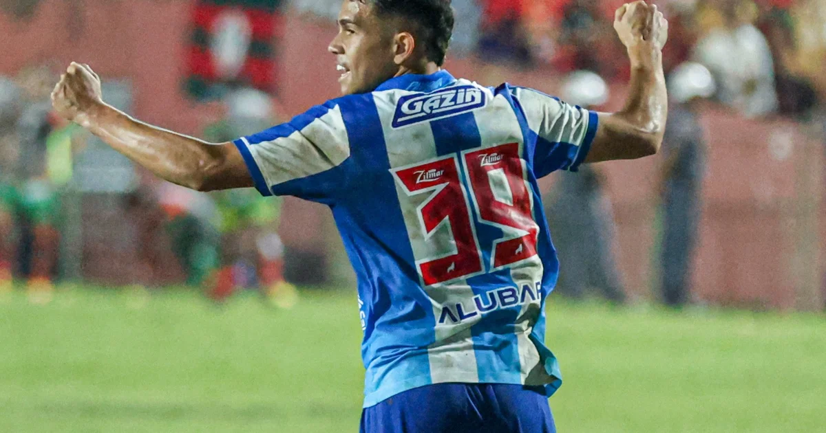 Volante adolescente de costas com camisa vermelha e preta nº18, contrato na mão, estádio lotado ao entardecer.