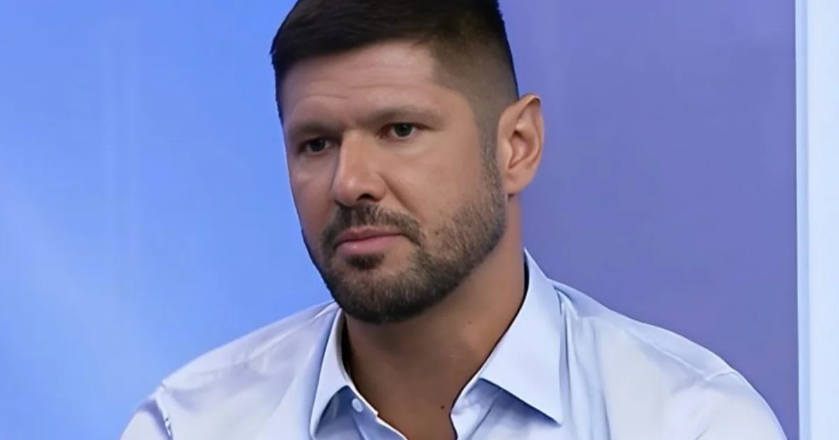 Ex-capitão no centro do estádio, bandeiras rubro-negras ao fundo e imprensa em primeiro plano, clima de expectativa e decisão.