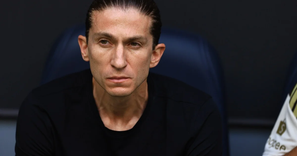 Ilustração editorial de estádio tenso: torcedores em vermelho e preto, técnico cabisbaixo, derrota do Flamengo e pressão sobre Filipe Luís