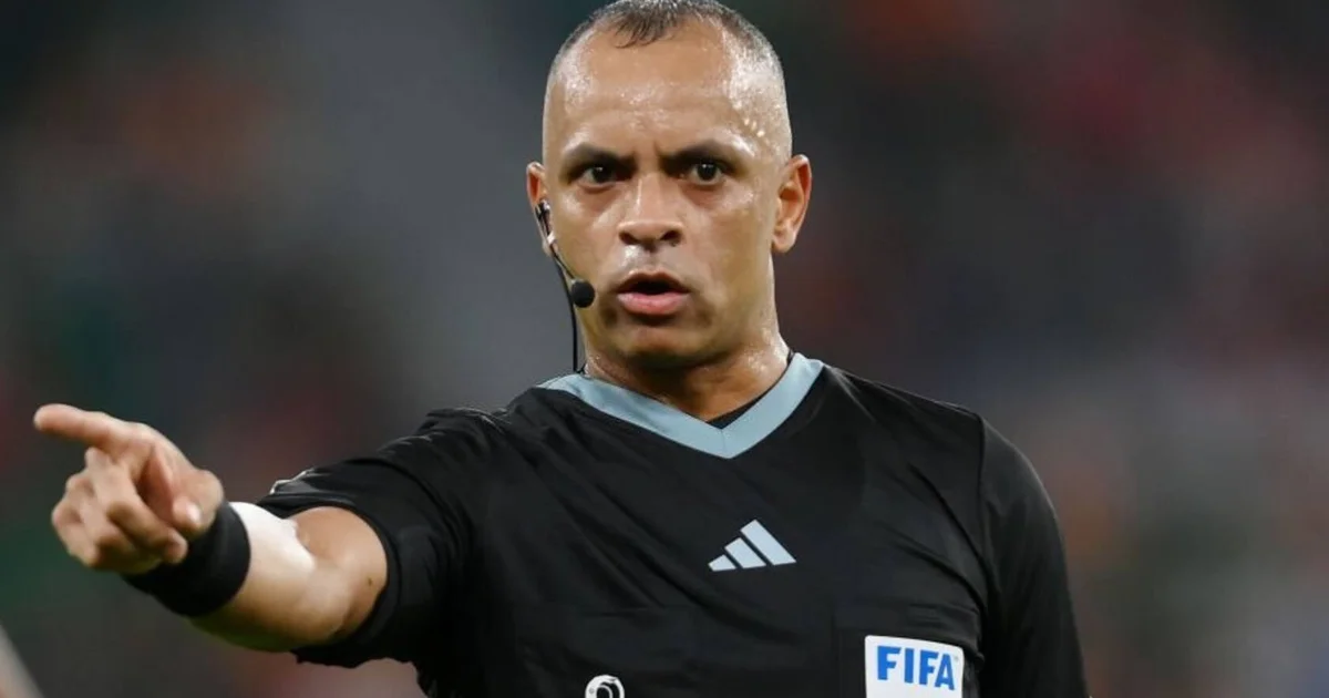 Árbitro de costas no Maracanã, apito erguido, bola em jogo e torcida dividida em cores do clássico