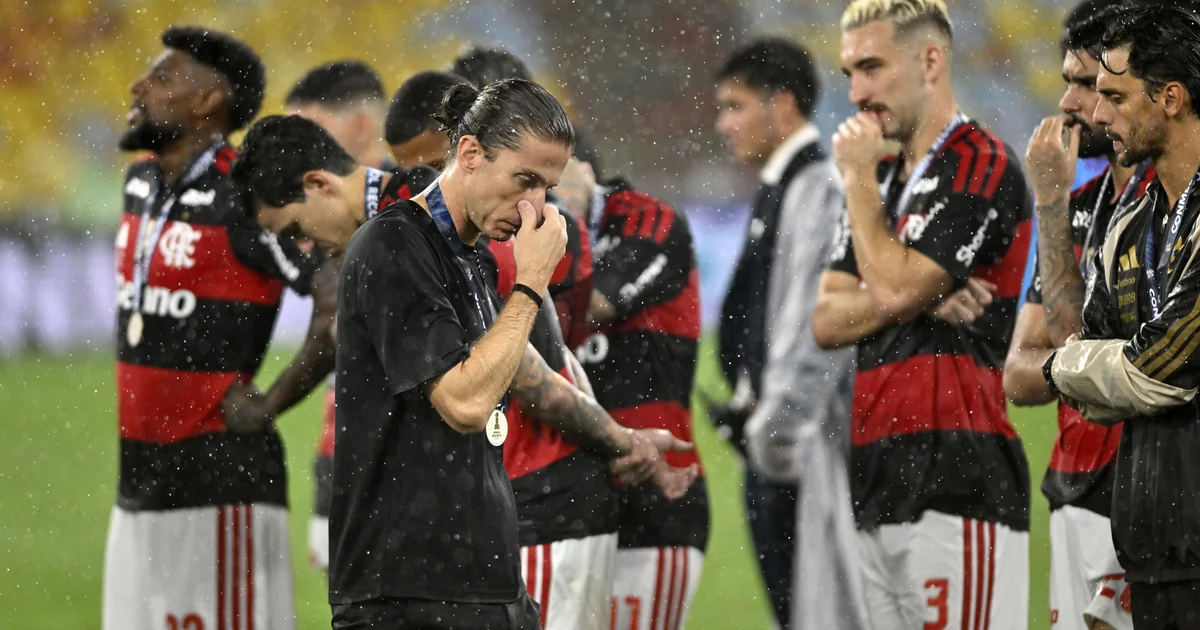 Técnico de costas no Maracanã-like, torcida rubro-negra vaiando após derrota por 3 a 2, clima de pressão e tensão.