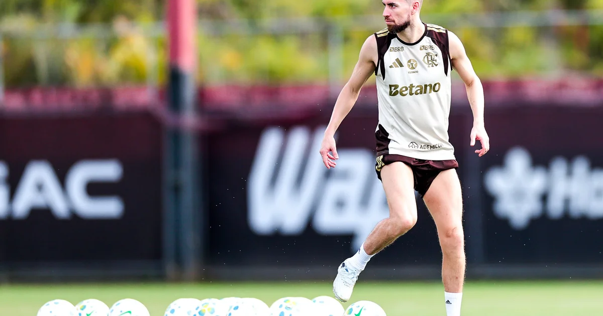 Maracanã à noite: torcida em vermelho e preto, banco com camisa vazia e fisioterapeuta cuidando de um meia lesionado, clima tenso.