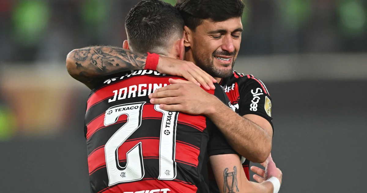 Estádio dividido: lado do Flamengo em tons dourados com pilha de moedas e torcida; lado adversário menor e frio; placar 25,7x.