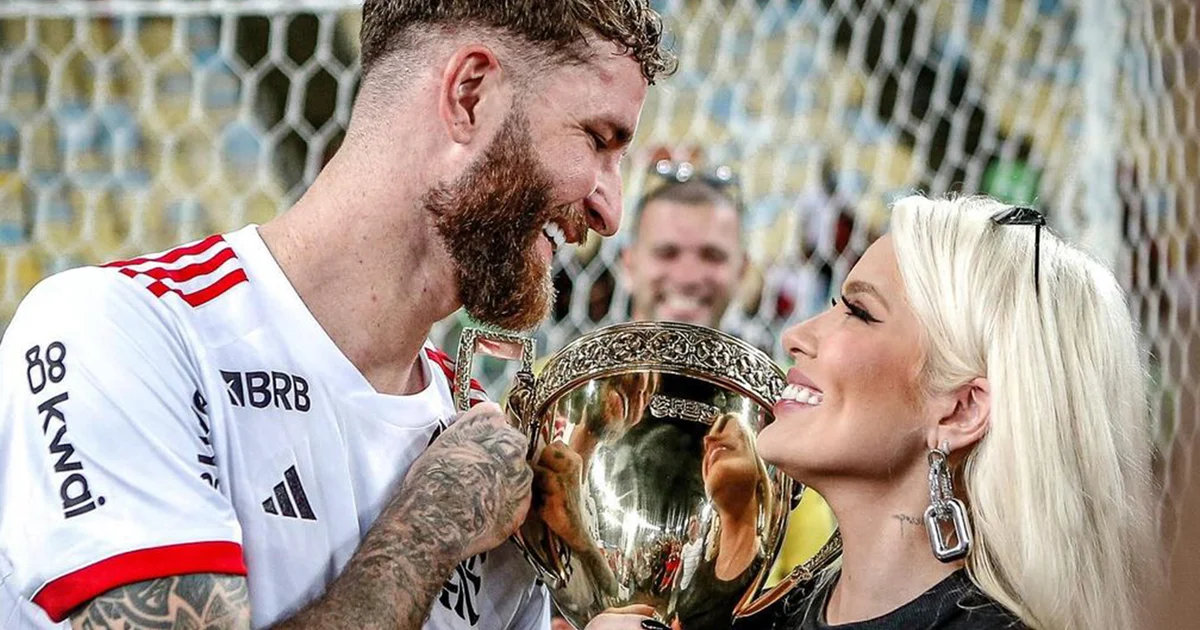 Casal anônimo sai de restaurante japonês no Rio à noite, flashes de paparazzi; ao fundo estádio iluminado em tons vermelho e preto, clima de futebol.