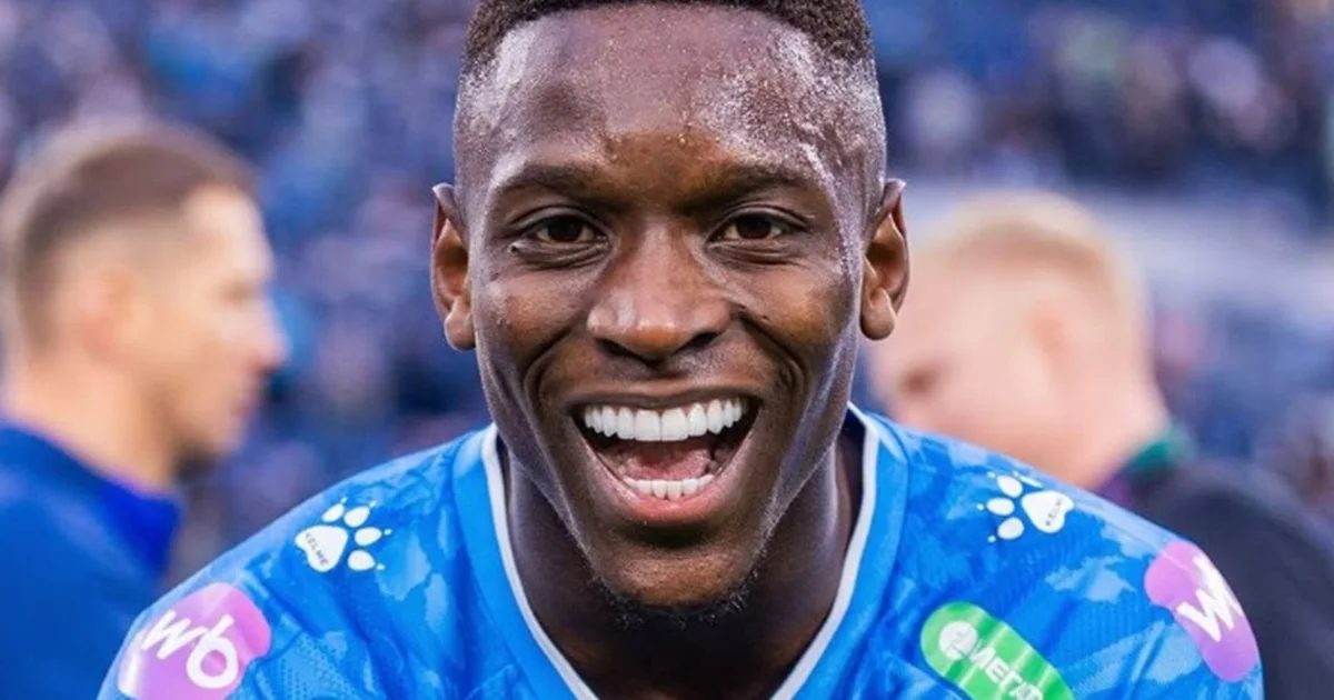 Torcida com bandeiras vermelho e preto, atacante sem rosto em voo para finalização, ícones de redes sociais sugerem rumor de transferência.