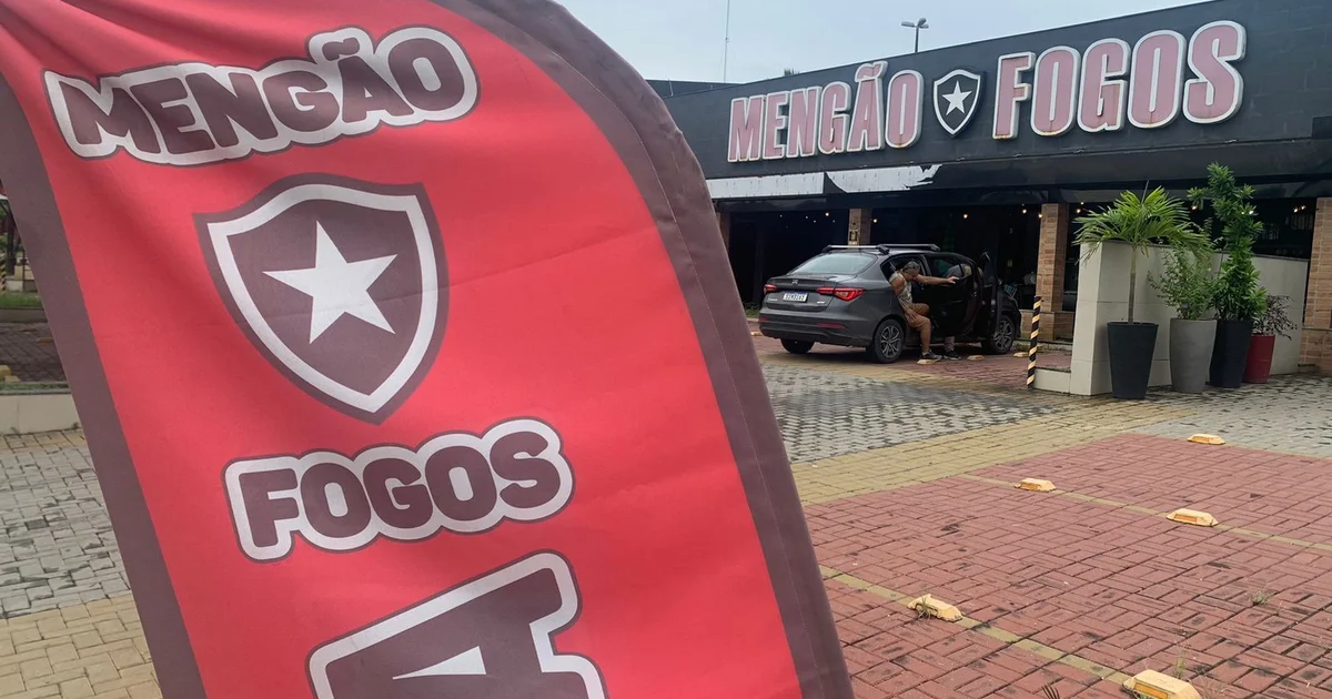 Fachada da loja 'Mengão Fogos' em Duque de Caxias com cores vermelho e preto e escudo genérico, pedestres curiosos antes do clássico.
