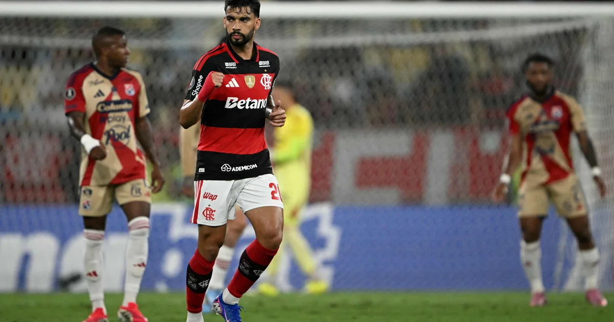 Paquetá comemora primeiro gol na Libertadores: chute cruzado na área, estádio lotado com bandeiras rubro-negras e goleiro mergulhando.