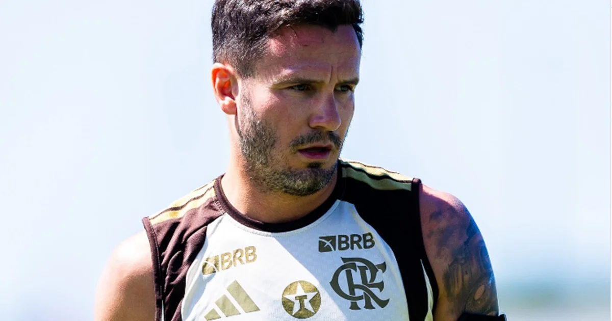 Meio-campista em reabilitação no gramado, tornozelo enfaixado, staff médico e técnico observando o retorno cauteloso do clube